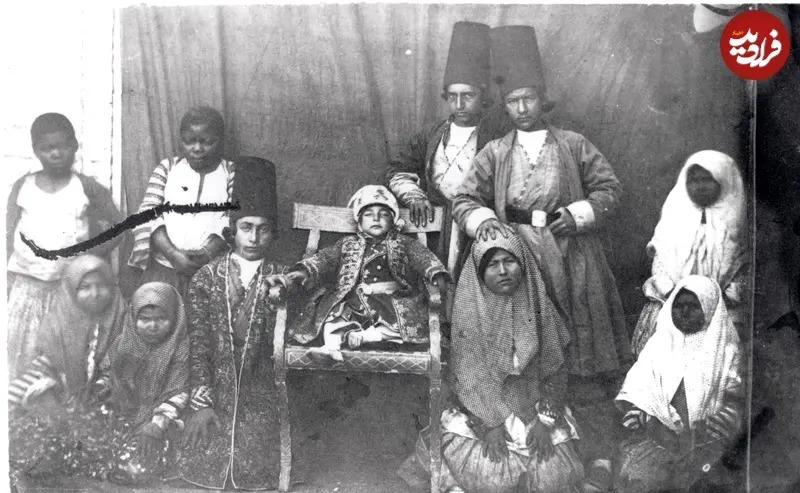 تصویری از یک کودک خردسال از خاندان سلطنتی قاجار را به همراه جمعی از کودکان دیگر که همراهان و خدمتگزاران او محسوب می‌شوند